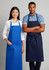 A blue bib apron and a navy bib apron on two models, one male and one female, standing side by side.