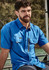 A man wearing a blue short sleeve outdoor shirt with two front pockets and a zip pocket. The shirt has a logo.