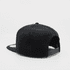 A black snapback cap with a flat peak and an adjustable strap at the back. It features a logo on the side.