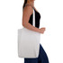 A woman carries a white cotton tote bag with long handles. The bag has a plain design and features a logo.