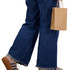 A small brown paper bag is held by a person dressed in blue denim jeans and tan platform shoes.