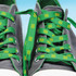 Green shoe laces feature a patterned design, threaded through grey sneakers. The laces are secured with a logo on them.