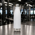 A drink bottle in sleek white with a stainless steel bottom, standing on a gym table. The bottle features a logo.