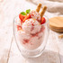 A dessert cup containing scoops of strawberry ice cream, topped with mint, strawberries, and wafer sticks.