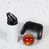 A drink bottle in white with a flip straw lid, accompanied by a red apple and a black gaming controller.