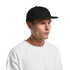 A black wool cap with a flat brim, worn by a person in a white T-shirt, featuring a logo on the front.