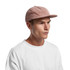 A cord cap in a soft pink hue displayed on a model wearing a white shirt. Features a flat brim and logo.