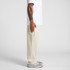 Cuffless track pants in a creamy hue, shown on a person alongside grey sneakers and a plain white shirt.