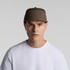 A brown 7-panel cap features a structured design and a logo on the front, worn by a model in a white T-shirt.