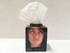 A tissue box with a black base and a white tissue protruding from the top, featuring a logo.