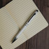 A silver and black Columbia Aluminium Pen rests on an open lined notebook. The pen features a sleek design and has a logo.