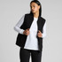 A black heavy canvas vest with a zip front, worn over a white long-sleeve shirt, featuring a logo on the garment.