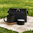 A coffee mug with a black upper and cork base, alongside a black container, both on a checkered blanket.