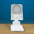 A white phone stand with an adjustable holder and a square base, set against a blue background.