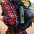 A drink bottle in green, featuring a logo, is attached to a backpack worn by a person in a checked shirt.