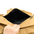 A hand reaching into a khaki kraft paper laptop backpack, revealing a black interior. The bag has a zipper closure.