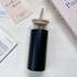 A drink bottle with a black base and clear glass top, featuring a wooden lid and a metal straw.