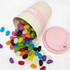A pink bamboo cup overflowing with colourful jelly beans, surrounded by scattered jelly beans on a white surface.