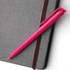 A bright pink plastic pen resting on a textured grey notebook, featuring a logo.