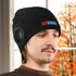 A black beanie with built-in speakers, featuring a logo and worn by a person in a warm, indoor setting.