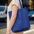 A person holds a reusable grocery bag in a deep blue hue, featuring shoulder straps and a simple design.