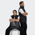 A black puffer vest featured on two models, one seated on a transparent chair and the other standing behind.