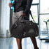 A black sport bag with a shoulder strap and a drink bottle, displayed in a gym setting. It features a logo.