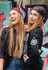 Two young women wearing caps, one in burgundy and the other in black, posing in front of a vibrant graffiti background.