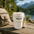 A drink cup in white, featuring a logo, placed on a wooden surface with a natural landscape in the background.