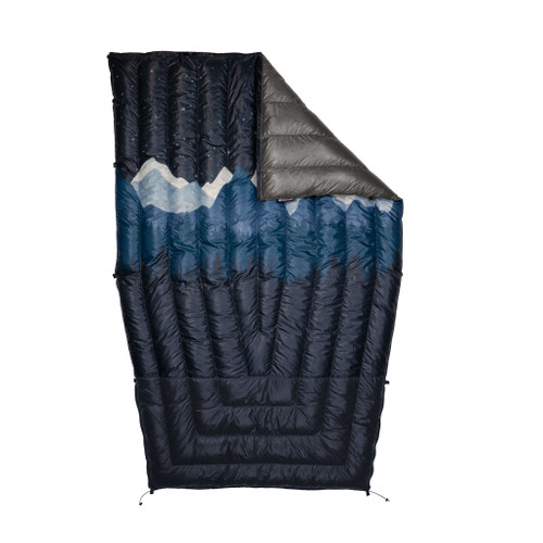 A flat lay custom revelation with a mountain range displayed on the front of the navy blue quilt with a corner folded displaying a charcoal liner.