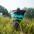 A man wearing a cap stands in a wildflower meadow, holding open a packable stuff sack featuring an aurora borealis print in teal and green over a starry night sky, with black-eyed Susans blooming in the foreground.