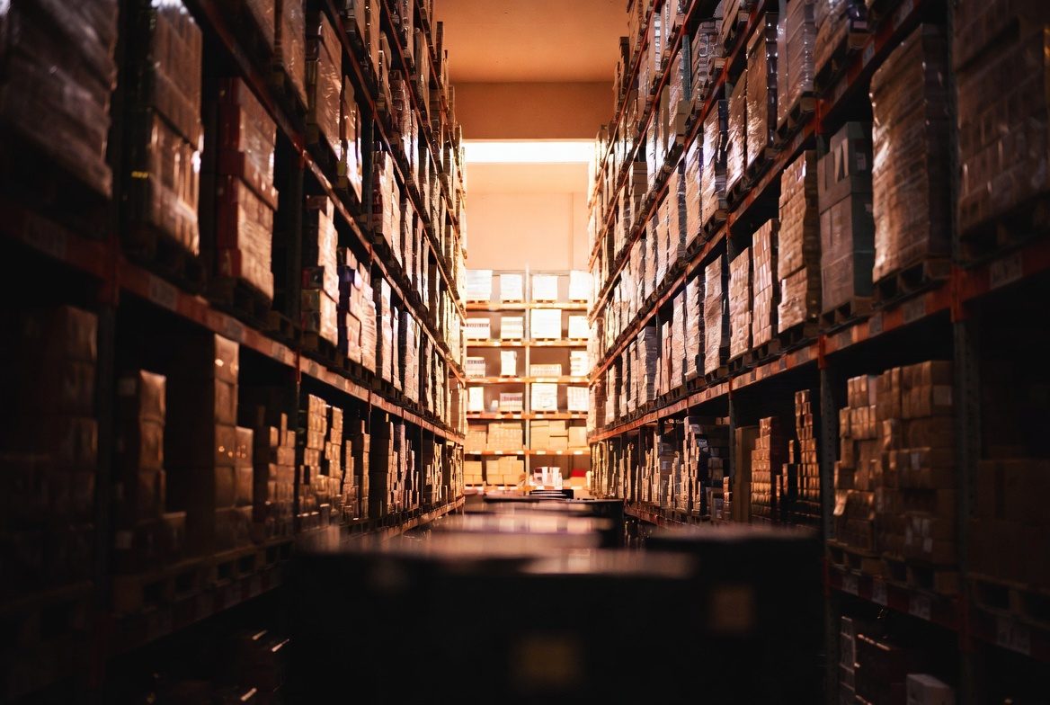 A warehouse aisle stocked floor to ceiling with cased inventory in warm light
