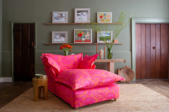 Maker and Son cosy comfy chaise longue upholstered in Anna floral fabric with pink and orange hues, set in a green-painted room. Maker and Son cosy comfy chaise longue upholstered in Anna floral fabric with pink and orange hues, set in a green-painted room.