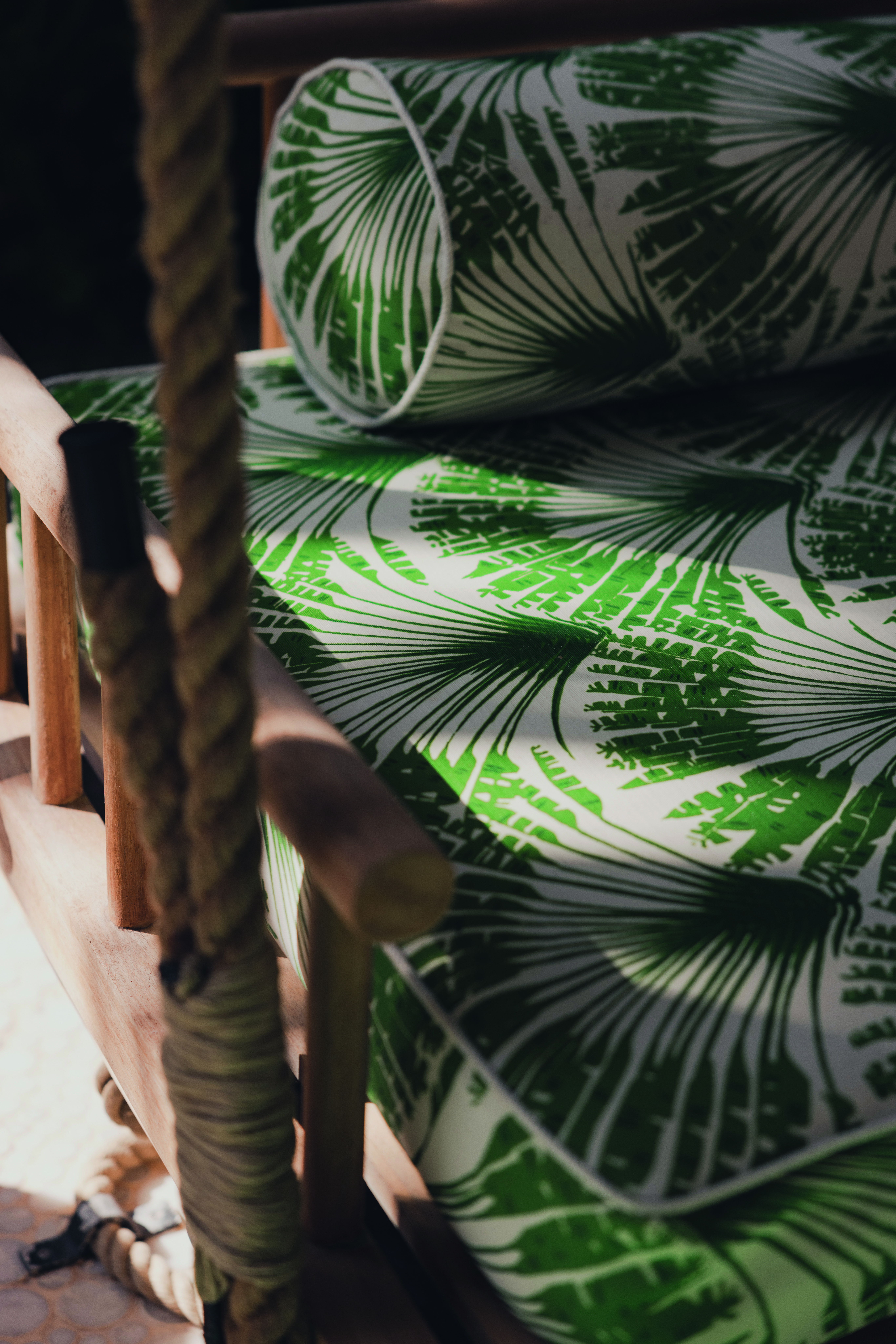 close view Outdoor rope-hung seating adorned with cushions upholstered in Brisa Verde, a feather fan print by Michael Szell. The design adds a rhythmic, graphic touch to the relaxed setting at Finolhu, blending durability with visual charm.