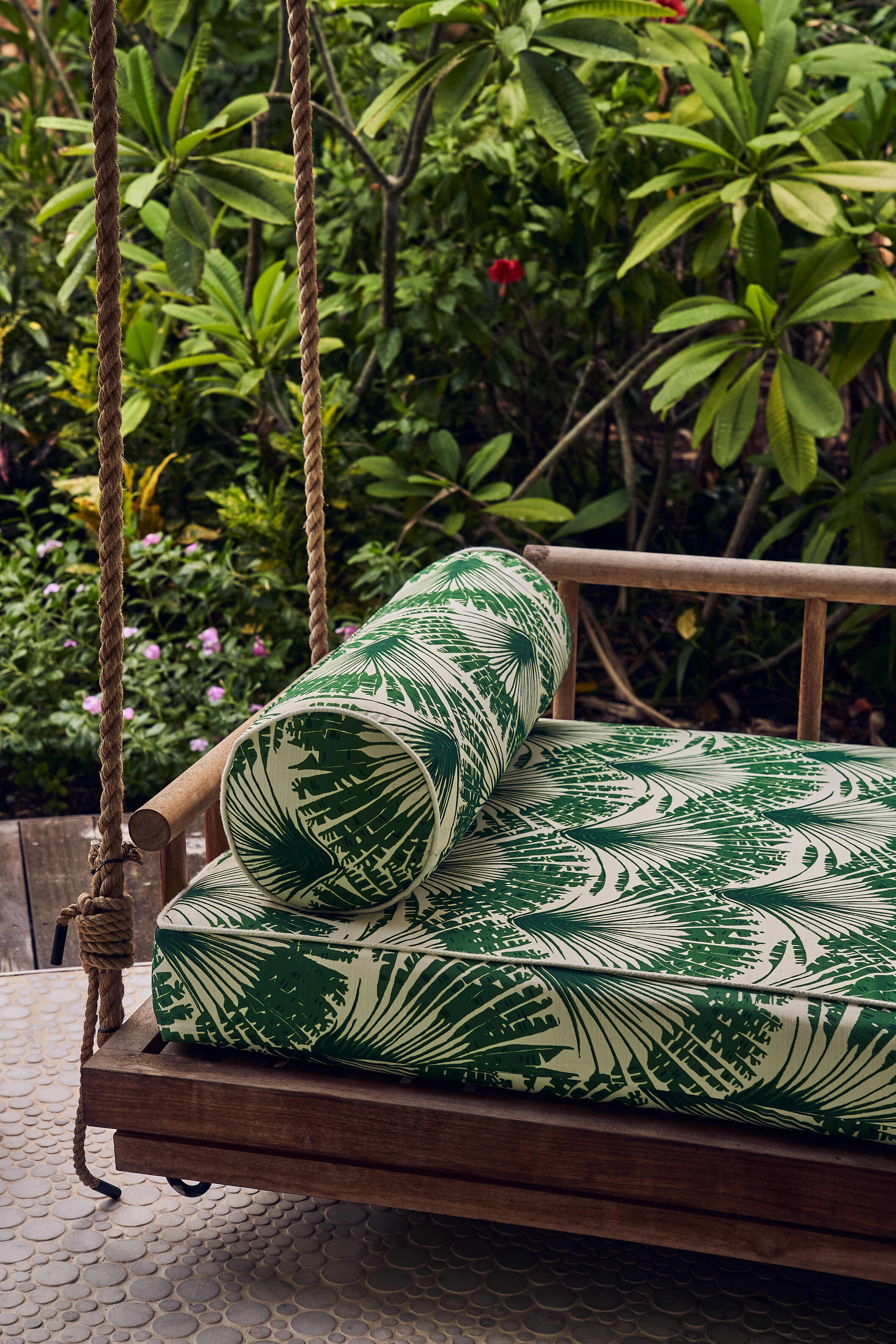 Outdoor rope-hung seating adorned with cushions upholstered in Brisa Verde, a feather fan print by Michael Szell. The design adds a rhythmic, graphic touch to the relaxed setting at Finolhu, blending durability with visual charm.