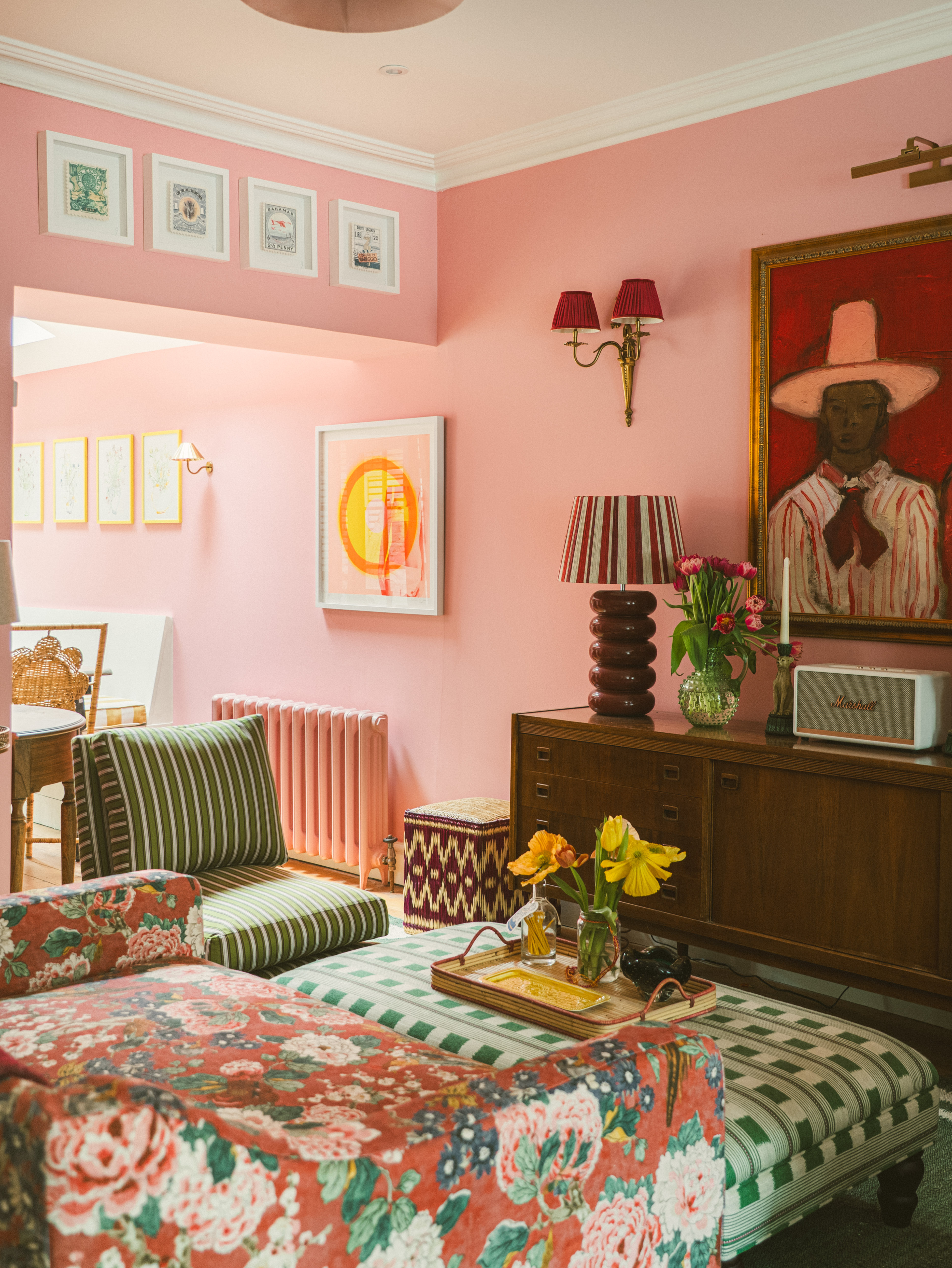 A peach-toned living space by Studio Flora London, featuring a green footstool in Lost and Found Indoor Woven by Kit Kemp, surrounded by collectables, vibrant accents, and layered textures.