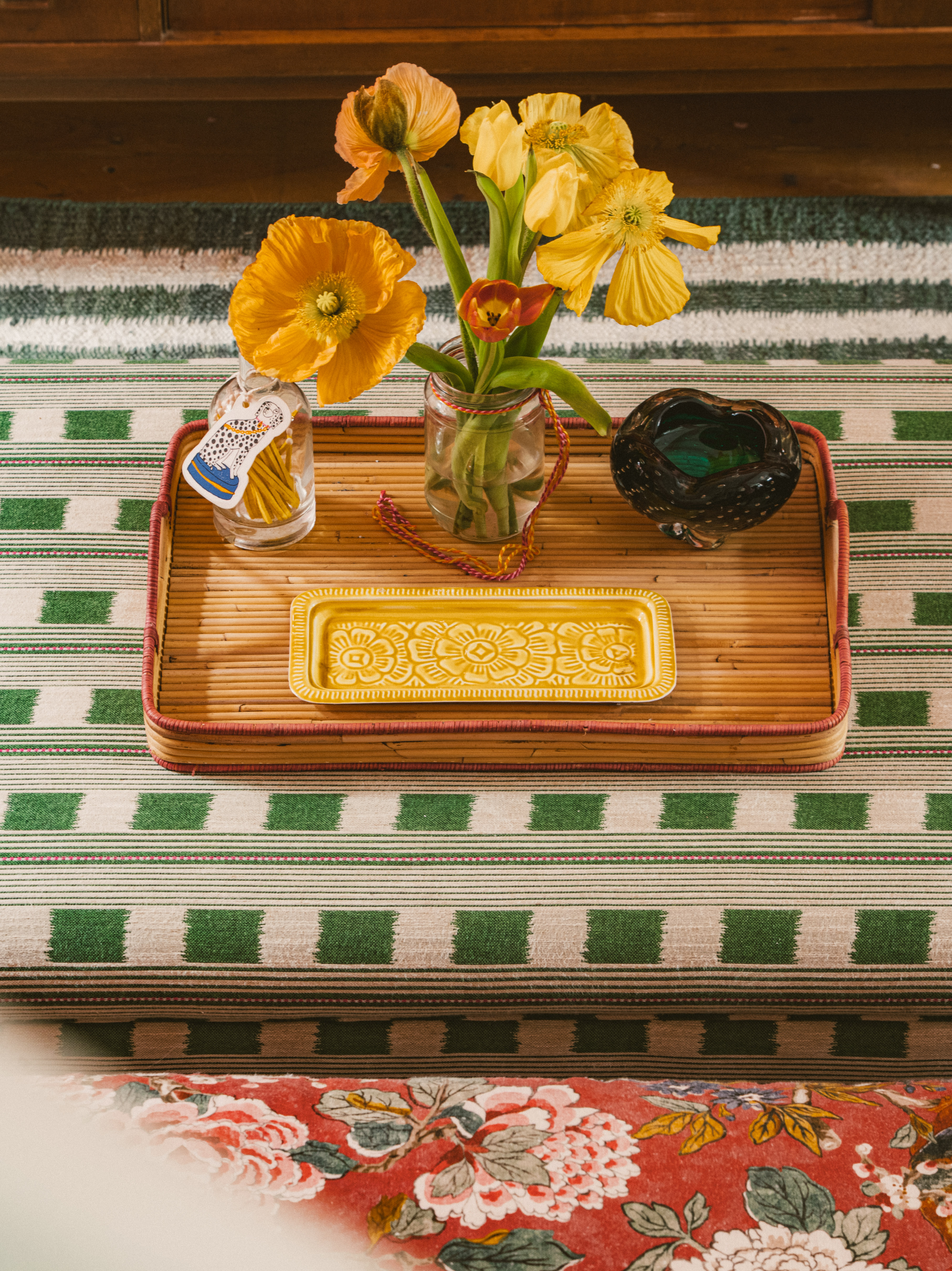 An above few of a footstool from an interior designed by Studio Flora London, upholstered in Lost and Found Indoor Woven fabric in green by Kit Kemp, surrounded by collectables, vibrant accents, and layered textures. Green and yellow fresh interior space and mix of patterns