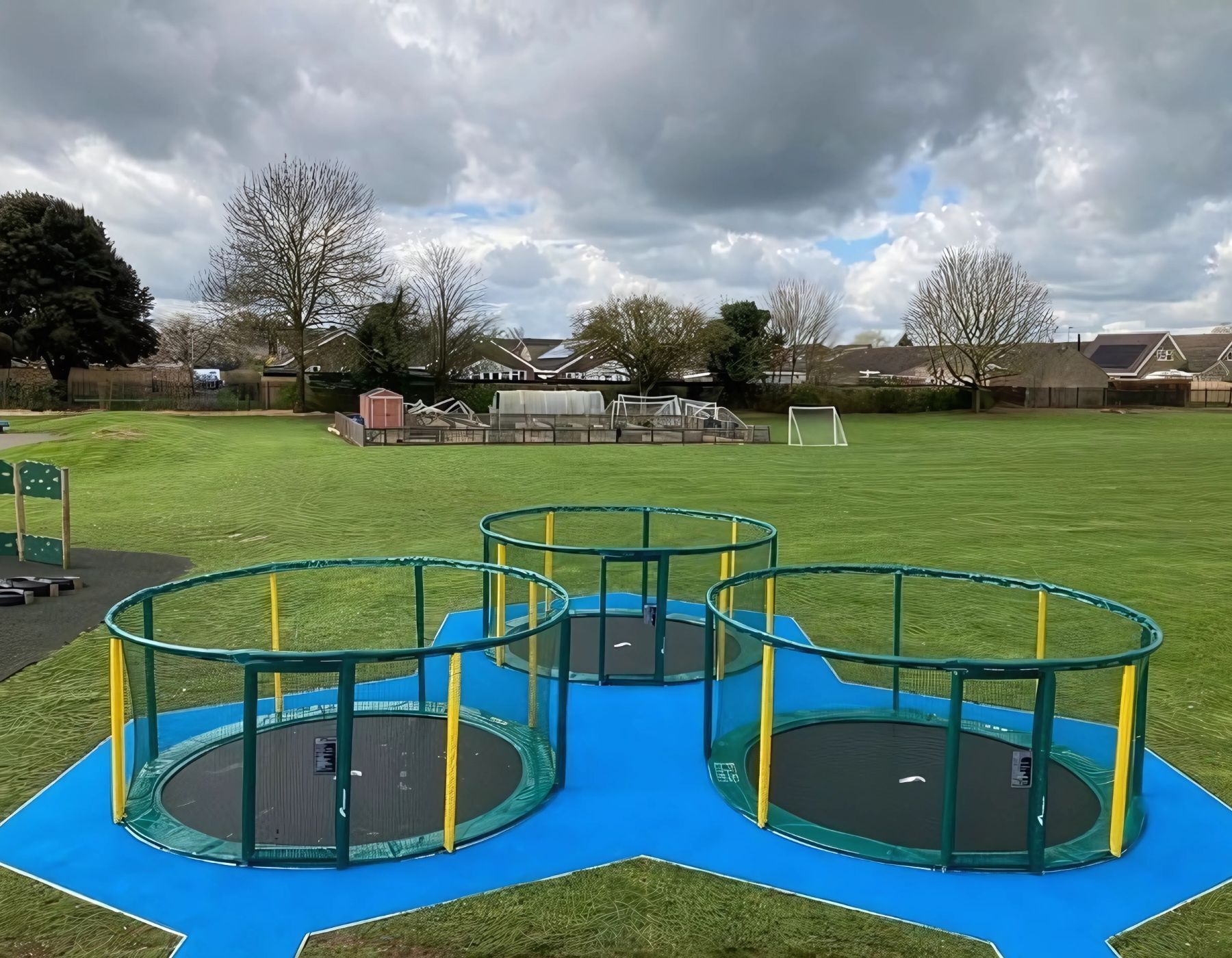 Three green and yellow Akrobat Gallus Flat Plus trampolines on a blue play surface