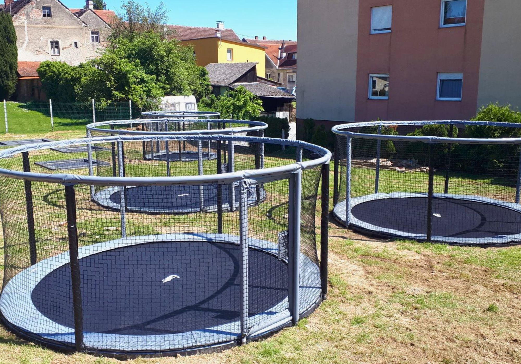 Several grey and black Akrobat Gallus Flat Plus in-ground trampolines in a garden