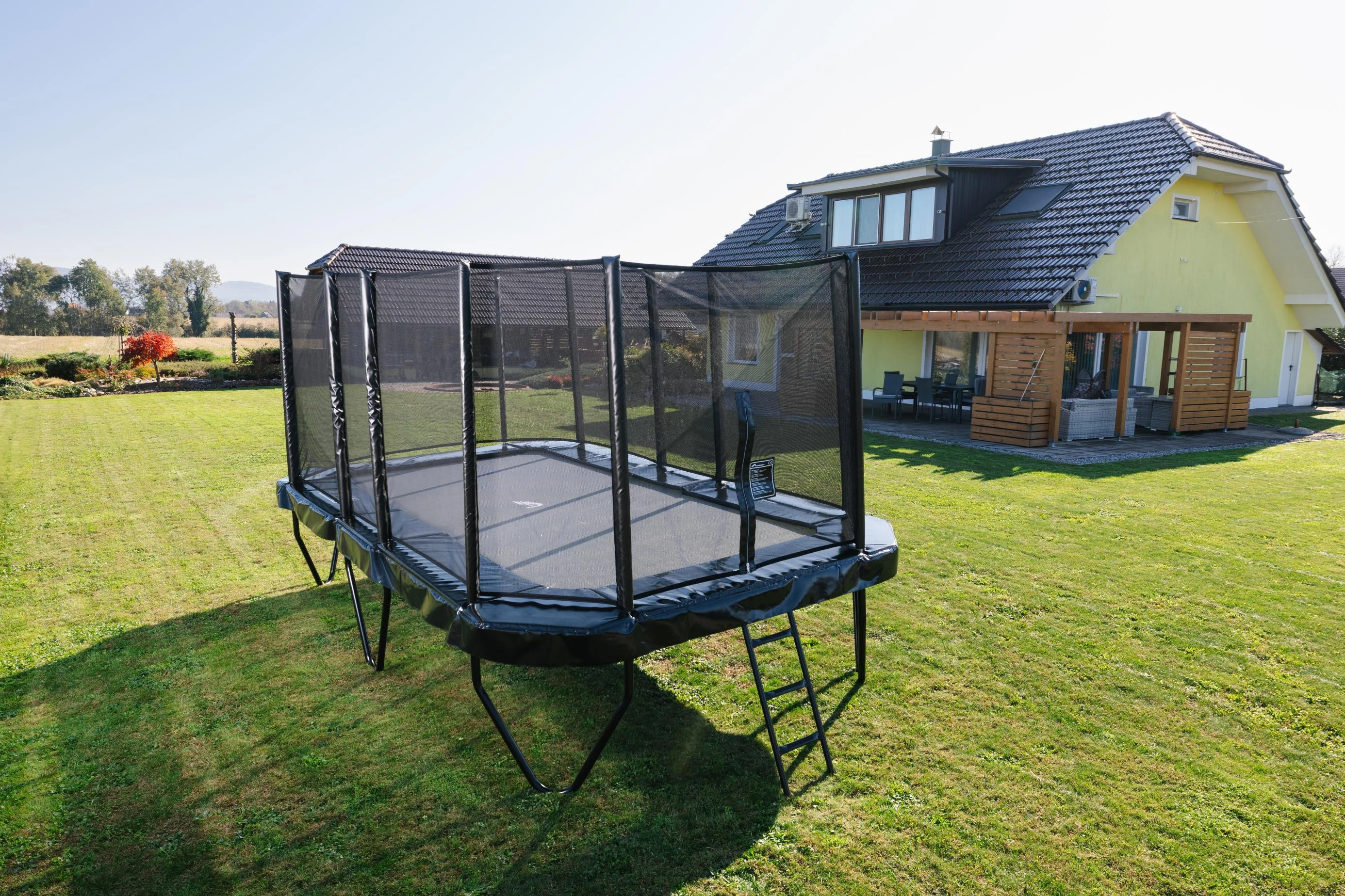 Akrobat Primus Challenger PLUS 17x10ft trampoline with safety net and ladder in a garden