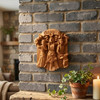 Celtic Goddess Brigid wood plaque hanging on a grey brick wall above a rustic wooden mantle, styled with a glowing white pillar candle and a potted ivy plant