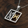 Pisces pendant: Two-tone silver and gold horoscope necklace resting on a rich, dark wooden surface