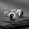 Yin Yang stud earrings for women, showcasing small, polished .925 sterling silver bezels resting elegantly on a dark, textured slate surface