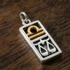 Libra charm at our pagan jewelry store in .925 sterling silver and 14k gold vermeil resting on a dark wood grain surface