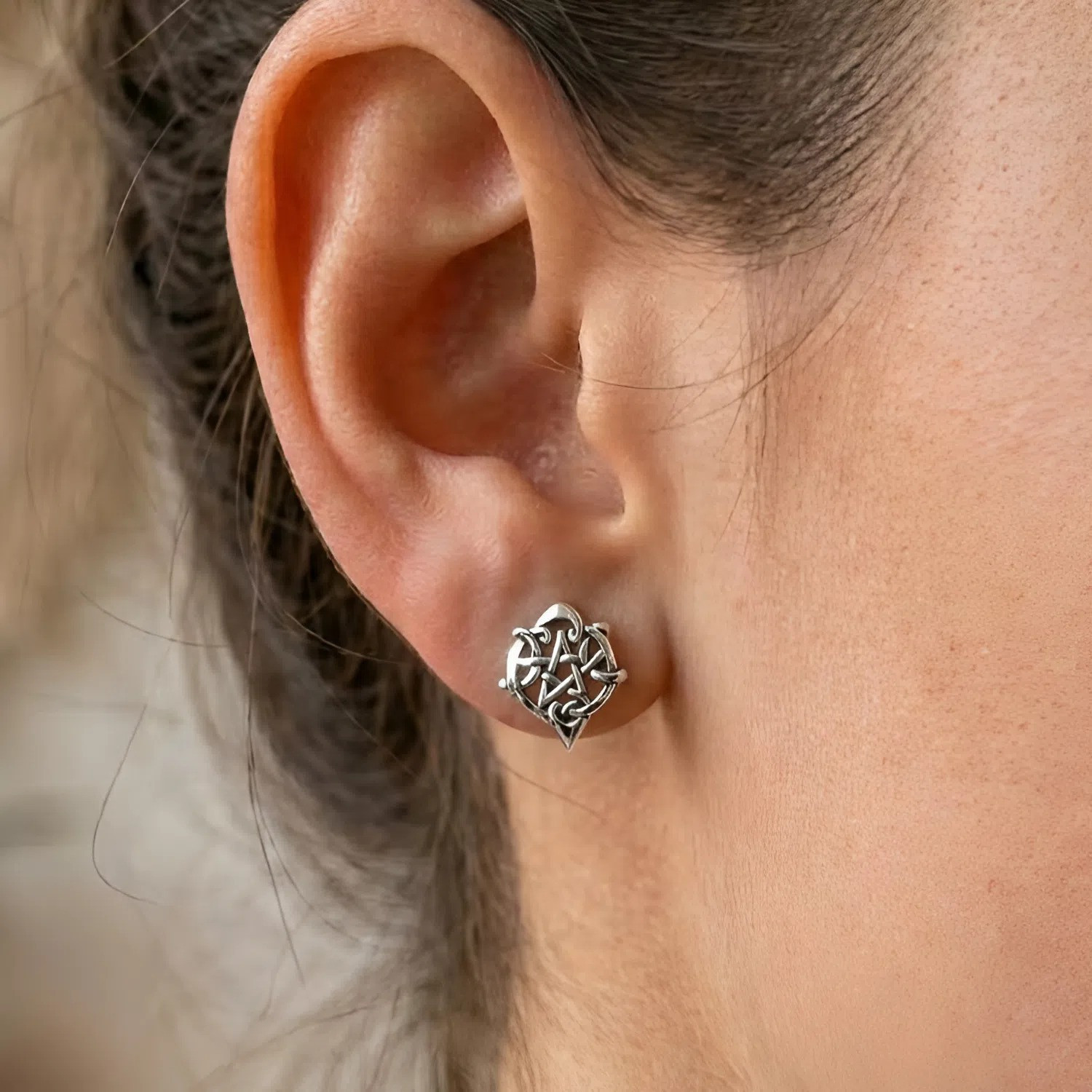 Earrings: Heart pentagram studs worn on a model's ear, showing the dainty size and polished silver finish