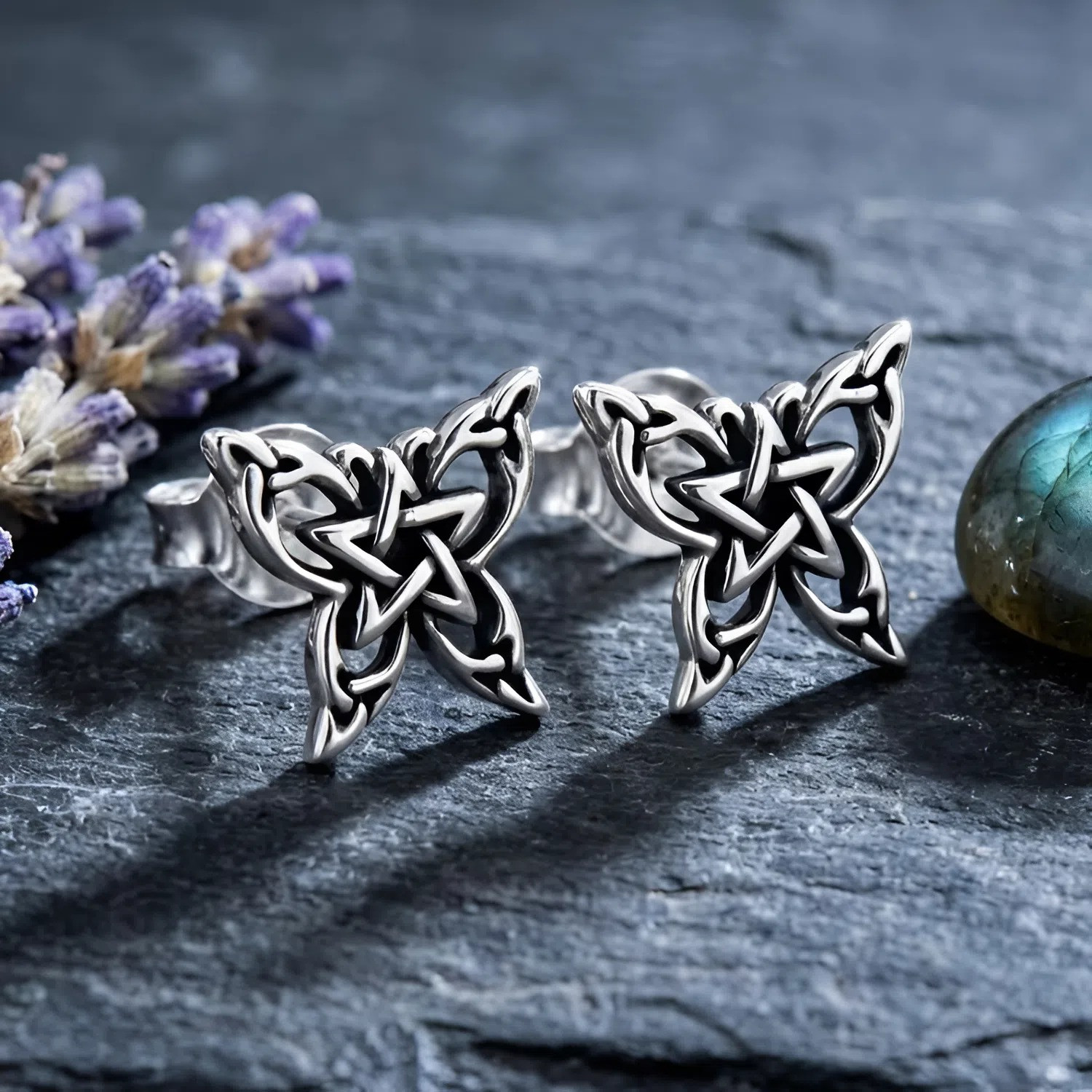 Pentagram earrings: Butterfly pentagram studs in .925 sterling silver resting on dark slate with lavender displayed at our Pagan store
