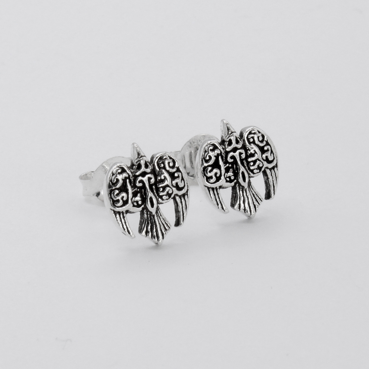 Morrigan Raven: Angled view of silver stud earrings highlighting the Celtic bird design on a white surface