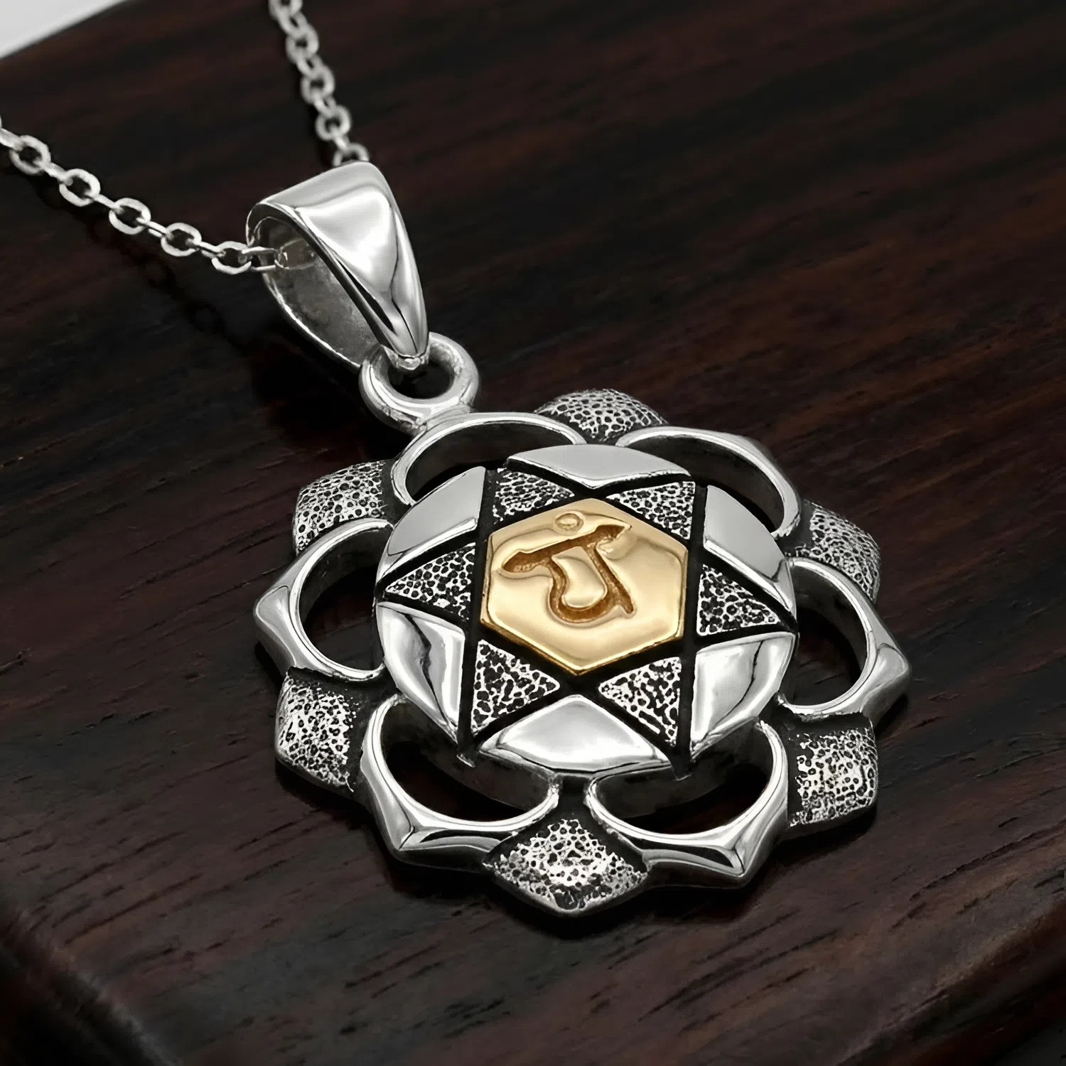 Chakra pendant for the Heart Chakra at our witch jewelry store resting on a dark wood background to highlight the silver and gold contrast