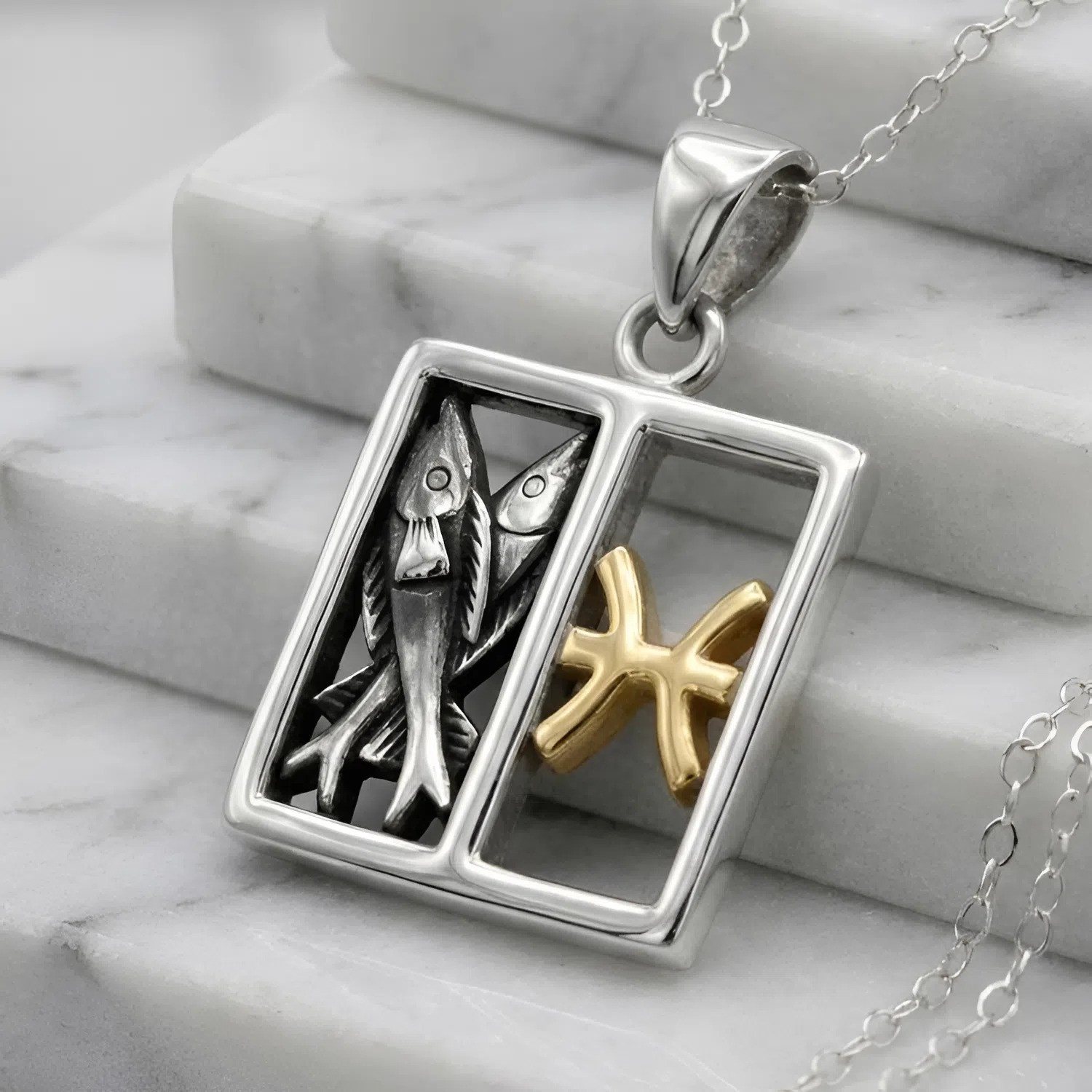 Sterling silver Pisces: Horoscope pendant featuring two silver fish and gold sign resting on white marble