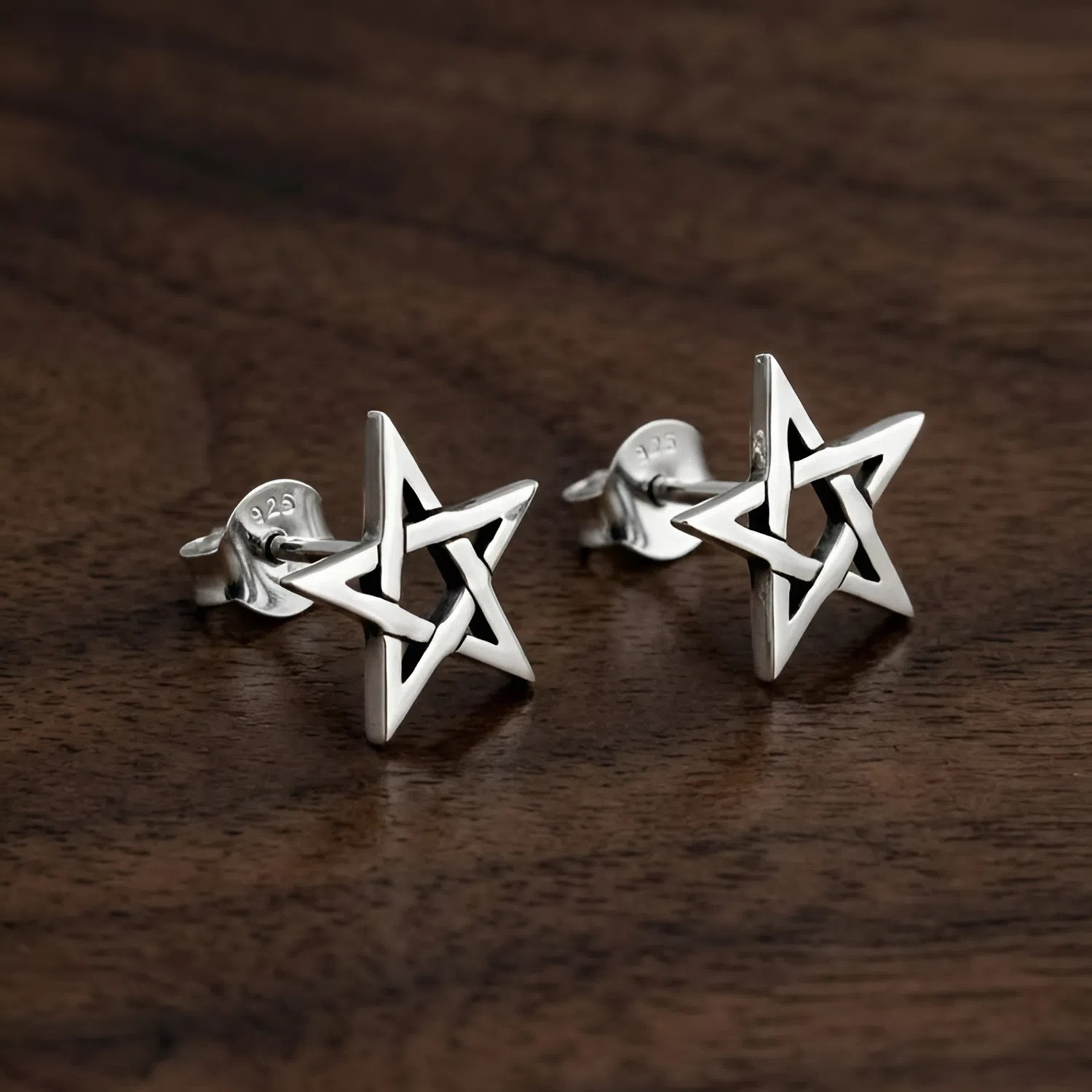 Star earrings designed as minimalist pentagram studs, resting elegantly on a warm, dark wood grain surface highlighting the polished silver finish